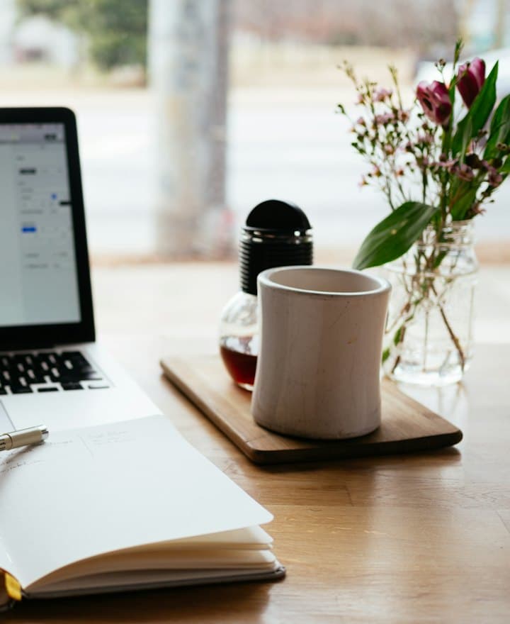 Notebook aberto em uma mesa com caderno e café